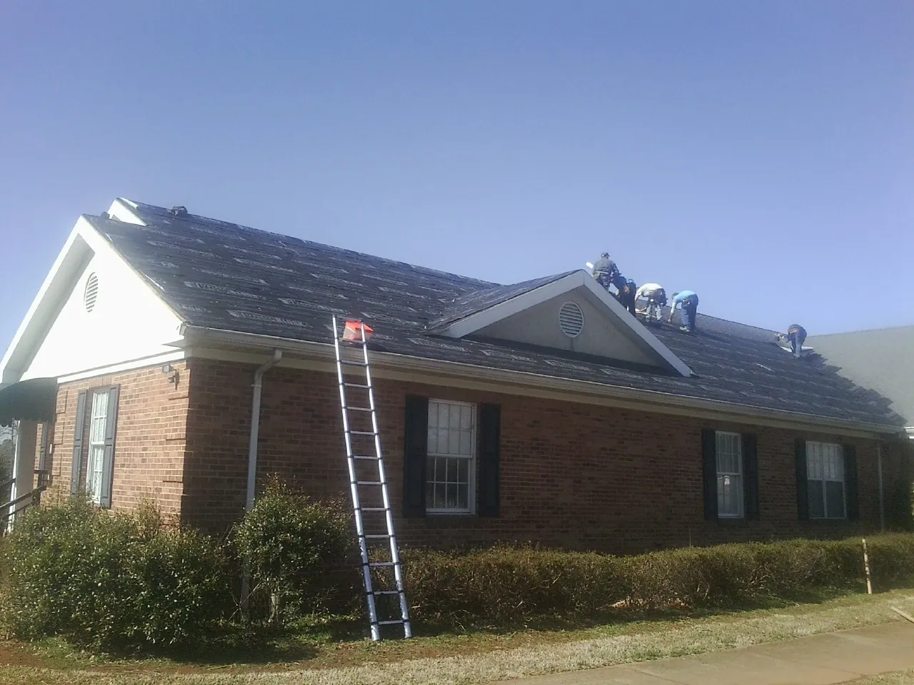 Crew tearing shingles off a brick ranch roof with a ladder set — Emergency Roof Repair work by our crew in Melrose