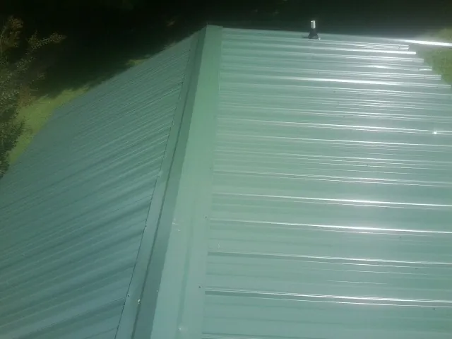 New green metal panels meeting at the ridge of a roof — Flat Roof Repair work by our crew in Melrose