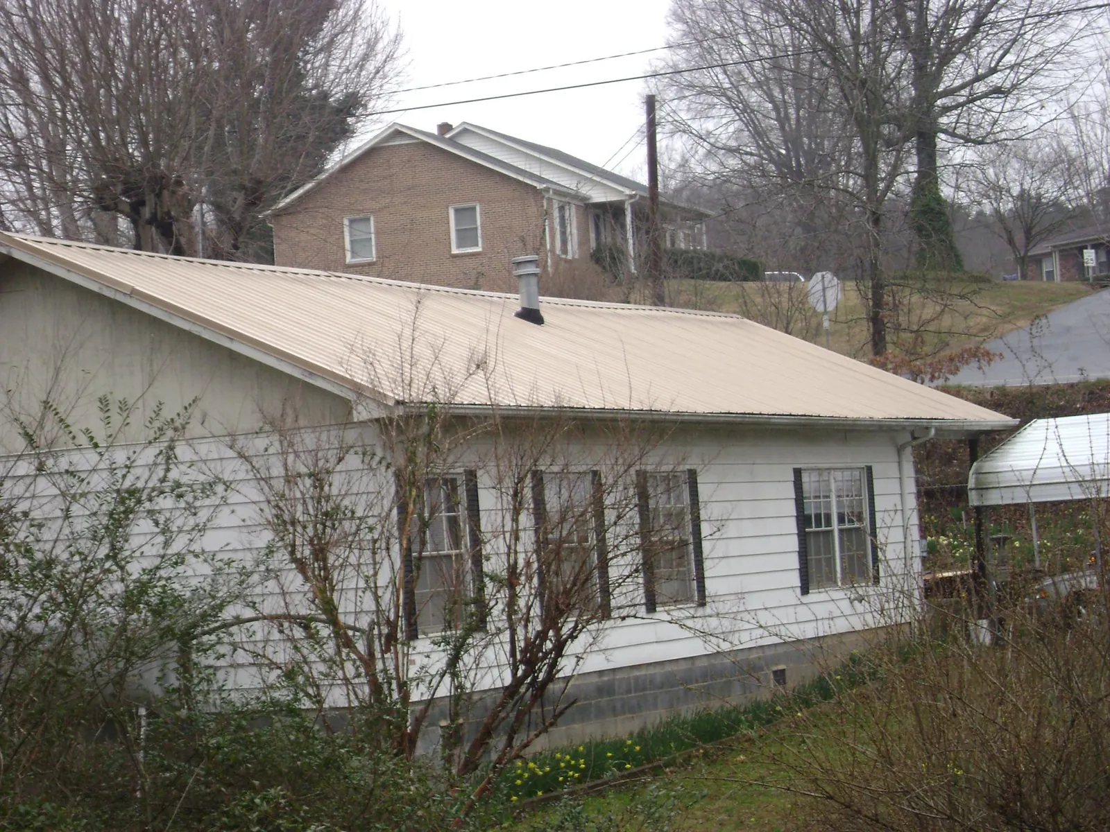 Tan metal roof on a white sided house set into a hillside — Commercial Roofing by Roofing Brothers in Melrose